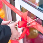 Режет ленточку на торжественном открытии магазина